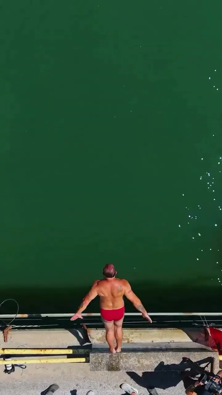 A swimmer poised above deep green water, from Tradita vazhdon