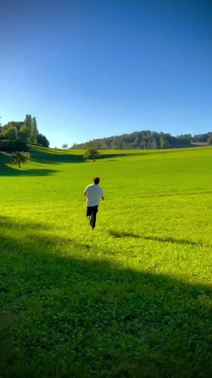 A lone figure crossing a vivid green field beneath a blue sky